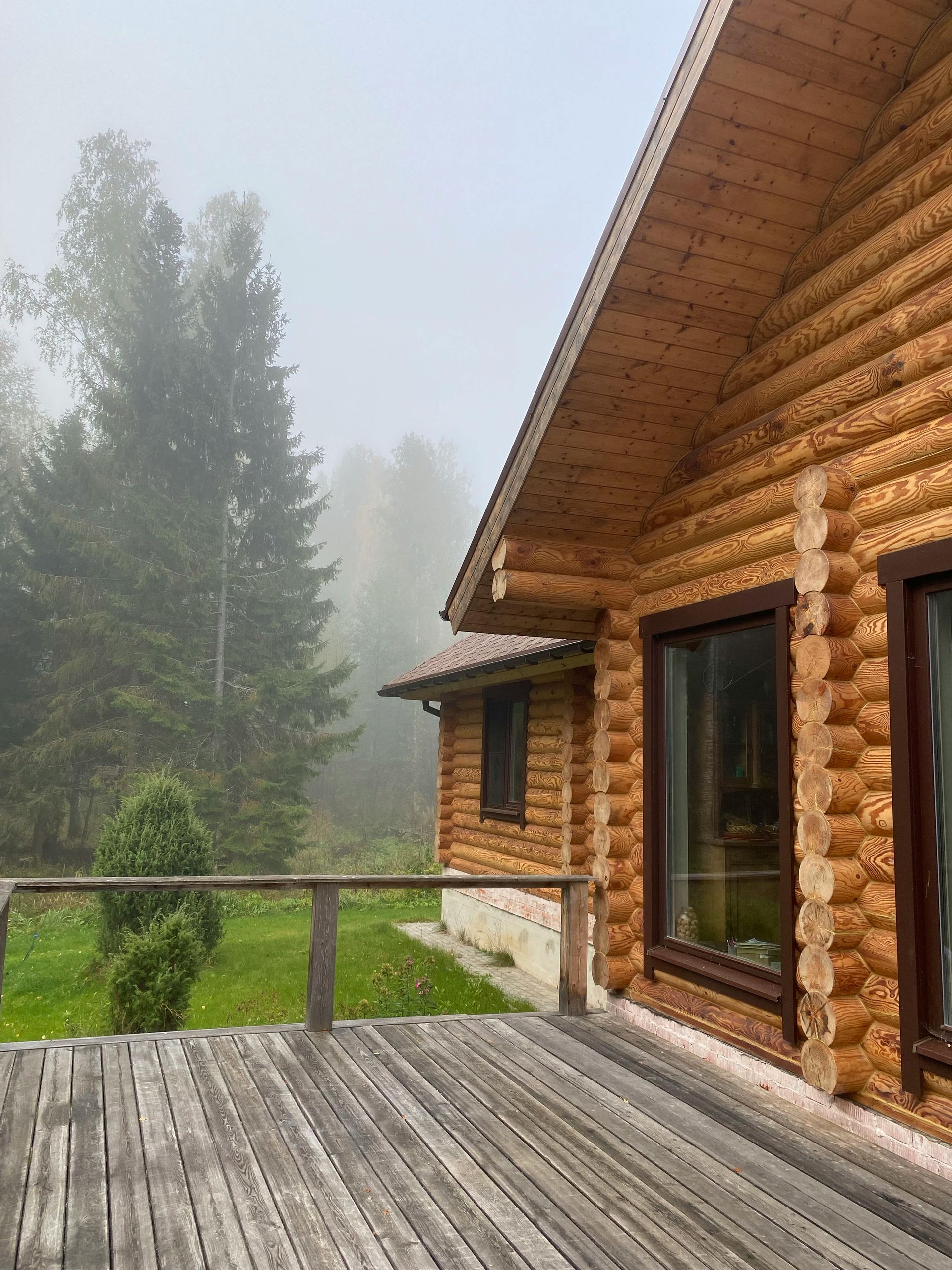Wooden cabin with a deck, surrounded by trees and fog.