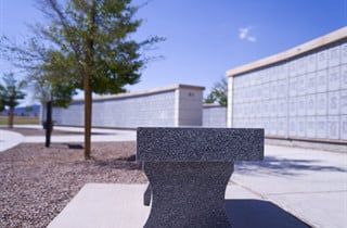 Concrete bench in a sunny courtyard beside a low stucco wall and trees