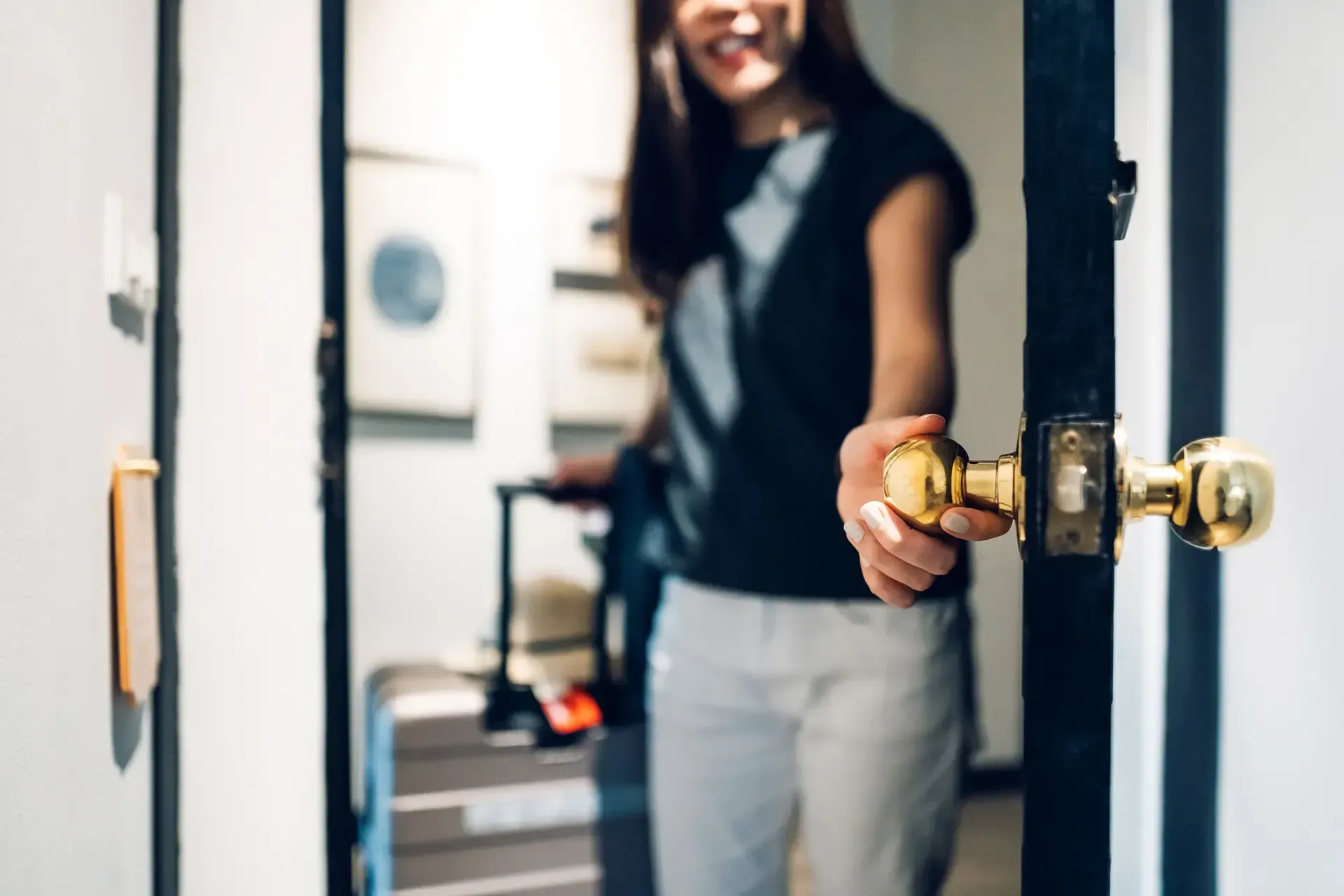 Una donna apre la porta di una camera d'albergo, trascinandosi dietro i bagagli. La luce del sole la illumina a fiotti; sorride.