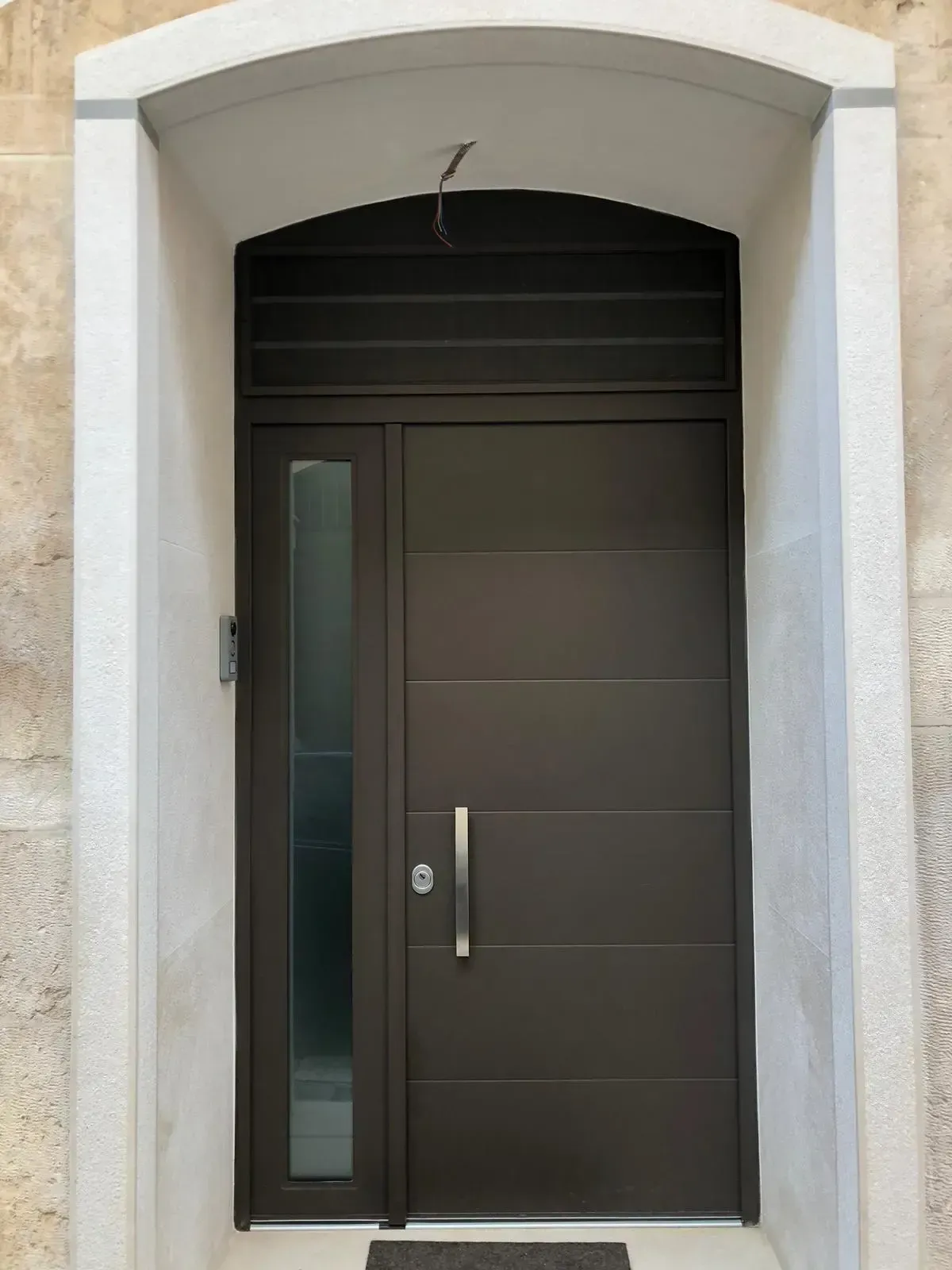 Porta d'ingresso marrone con finestra laterale in un portale in pietra.