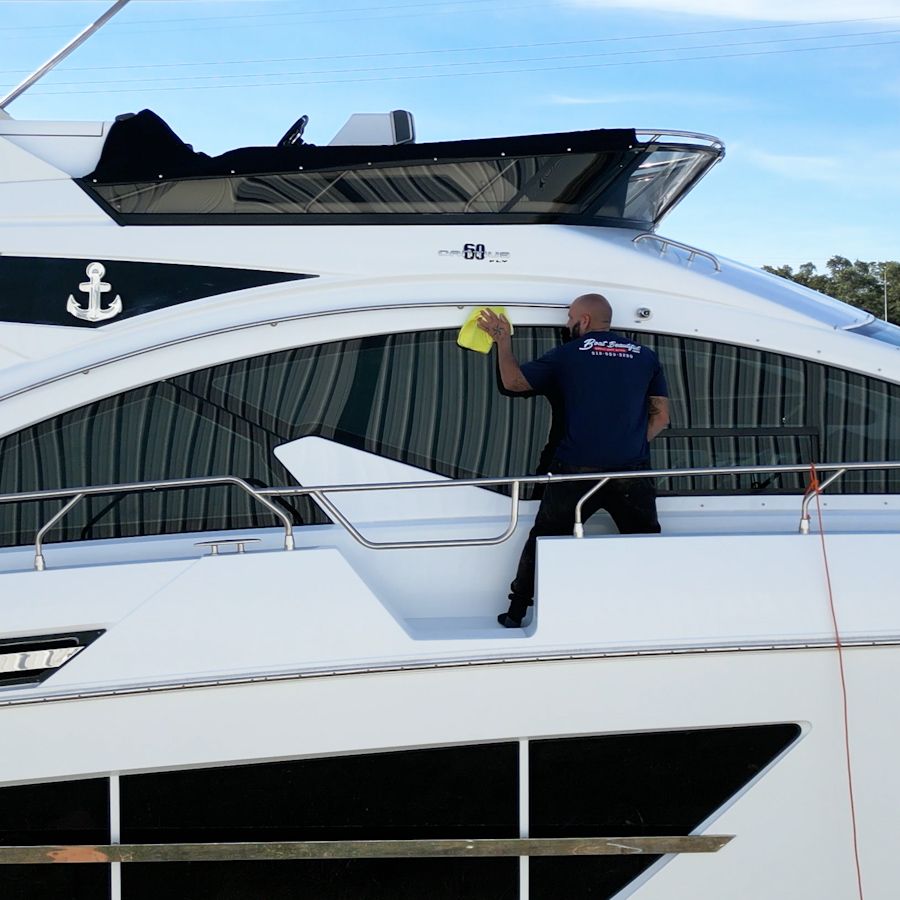 Man kneeling on a white boat deck, polishing it with a machine. Another man works below.