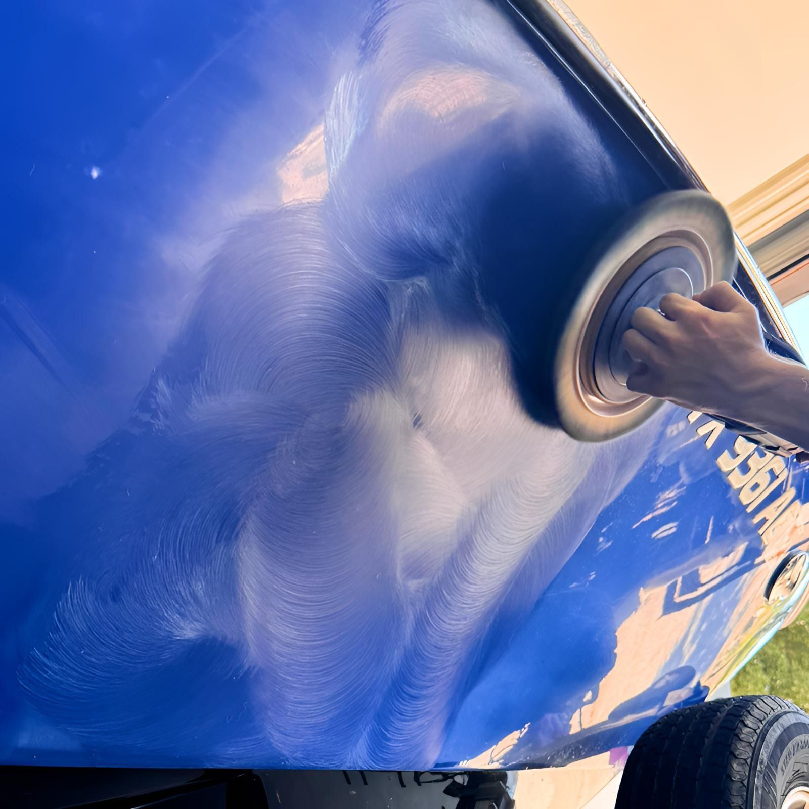 Person using a power buffer on a blue boat hull, creating a shiny surface with swirling patterns.