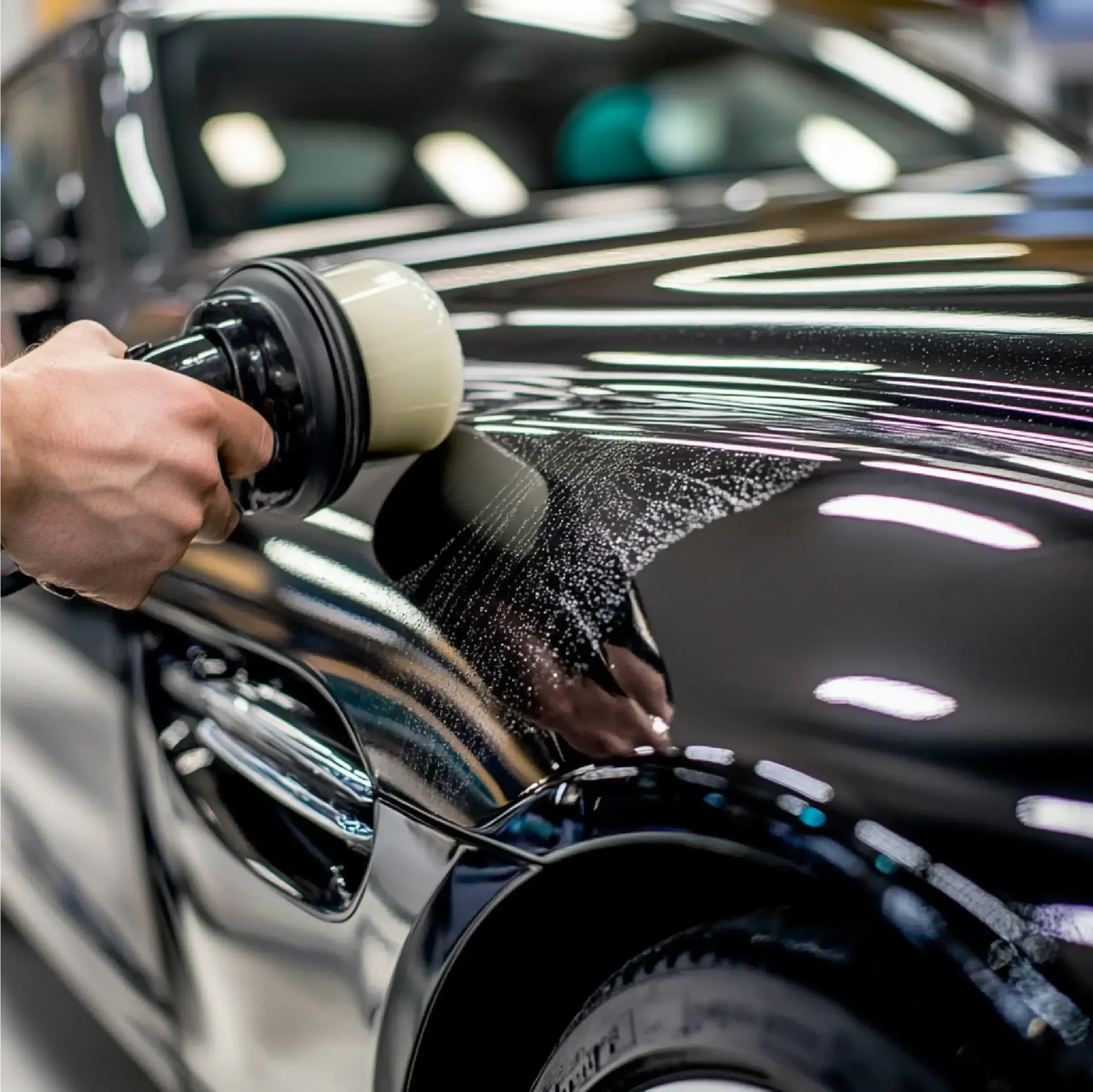 A person polishing a shiny black car with an electric polisher.
