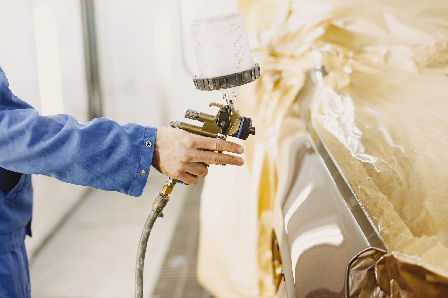Person spray-painting a gold car in a workshop, with a spray gun and blue sleeve visible