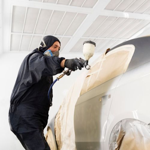 Man steam cleaning a car interior. He uses a steamer on the console. There are cleaning supplies nearby.
