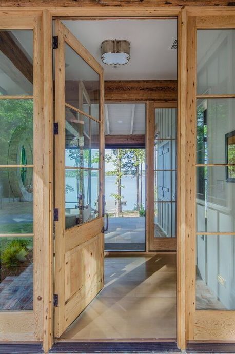 Open wooden door in a rustic foyer looking out onto a bright, lakeside porch.