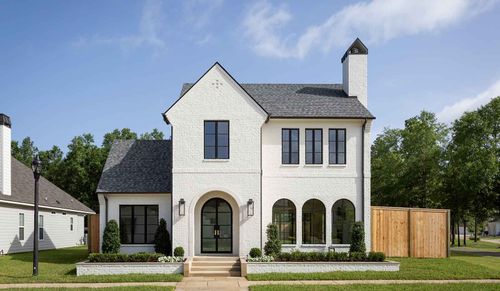 A two-story white brick house with a dark gabled roof, an arched entryway, and dark-framed windows under a clear blue sky.