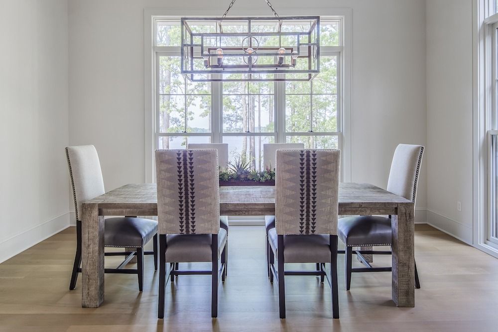 A rectangular wooden dining table with six chairs and a geometric metal chandelier, set in a bright, modern room.