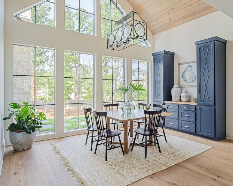A bright dining room with large windows, a square wooden table, four dark chairs, and navy blue built-in storage cabinets.