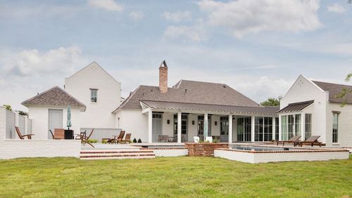 A white, multi-gabled house with a covered patio, brick accents, and a grassy backyard under a partly cloudy sky.