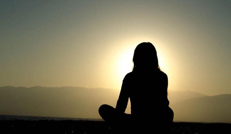 A silhouette of a woman sitting in a lotus position at sunset.