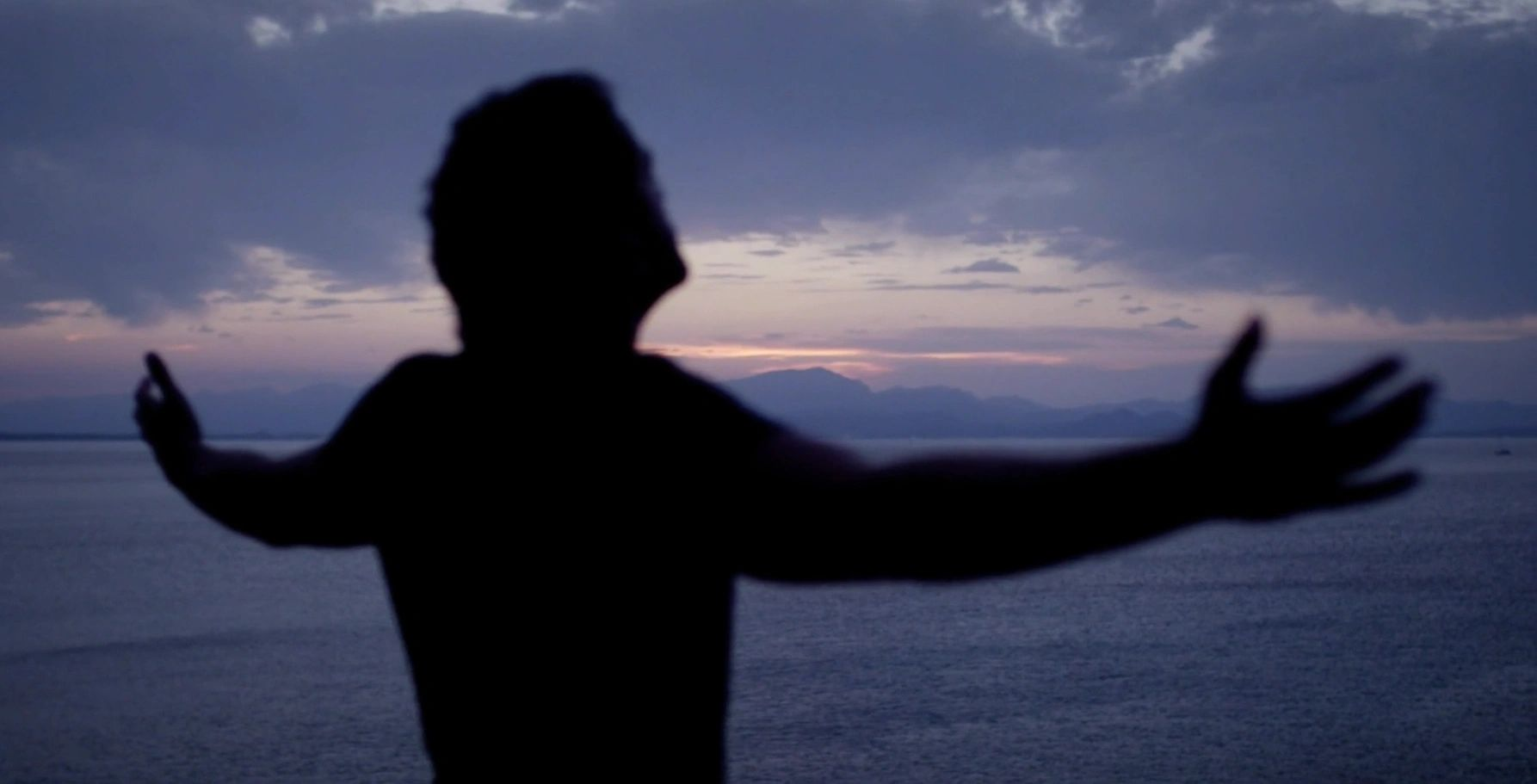 A silhouette of a man with his arms outstretched in front of the ocean.