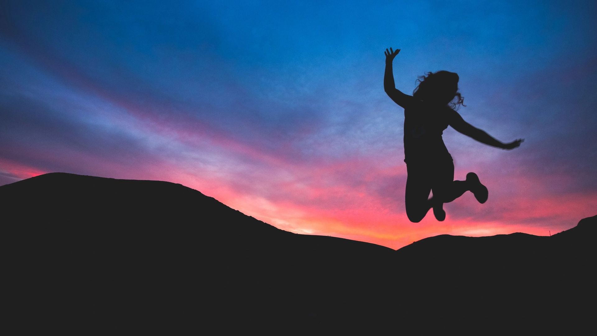 A silhouette of a woman jumping in the air at sunset.