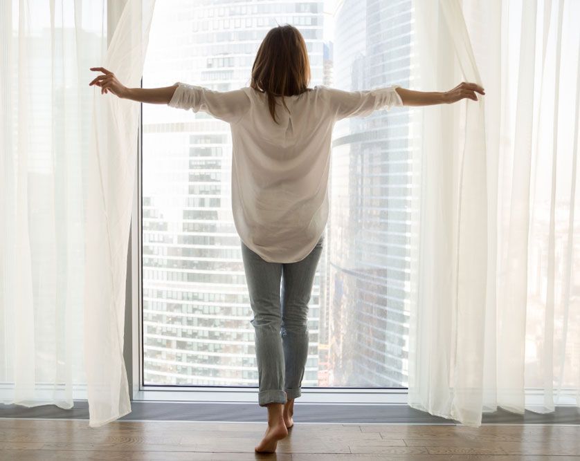 A woman is standing in front of a window with her arms outstretched.