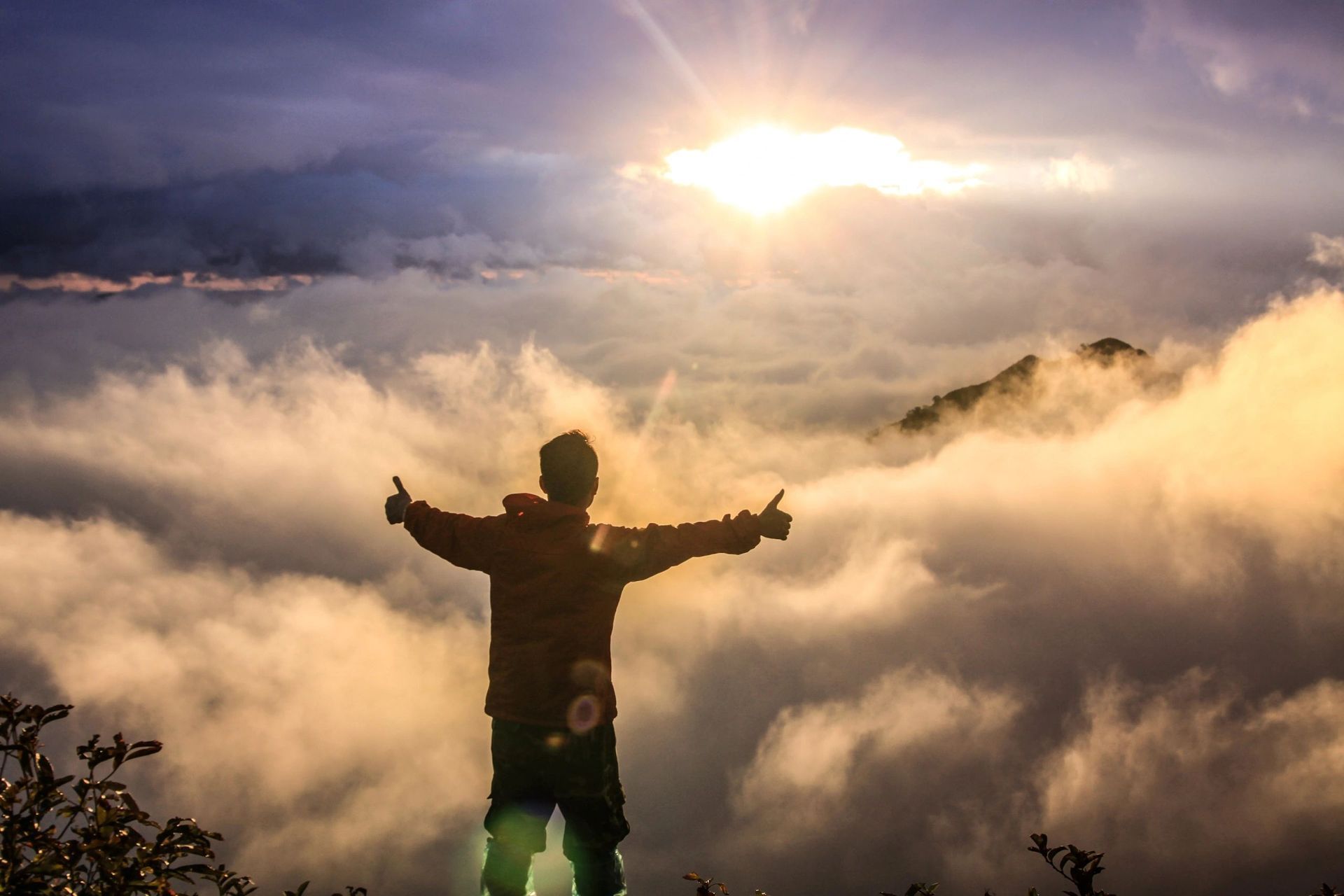 A man is standing on top of a mountain with his arms outstretched.