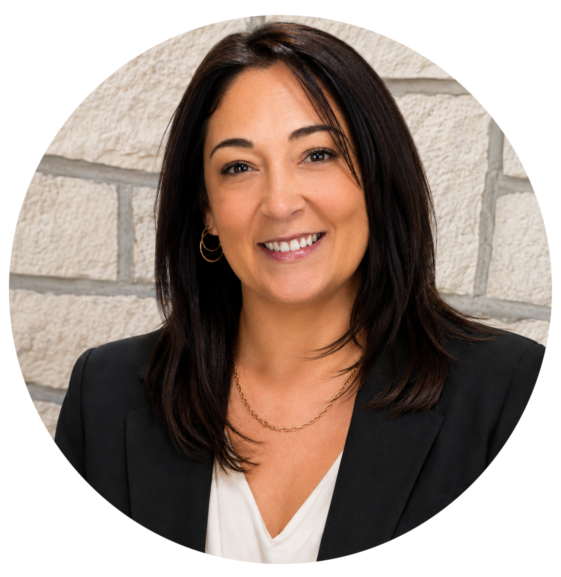 A woman in a black blazer is smiling in front of a brick wall.
