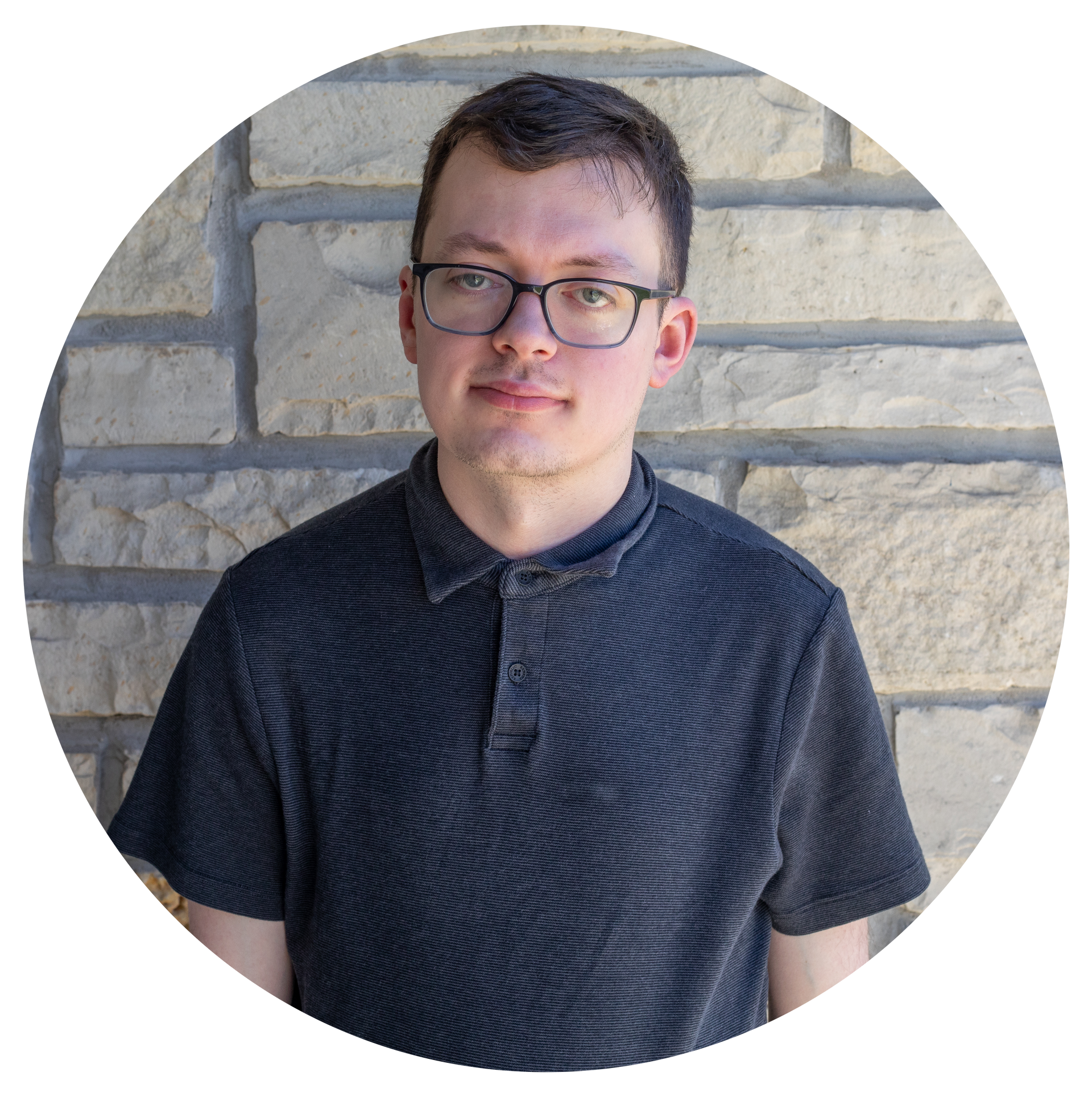 A man in glasses and a black shirt is standing in front of a brick wall. 