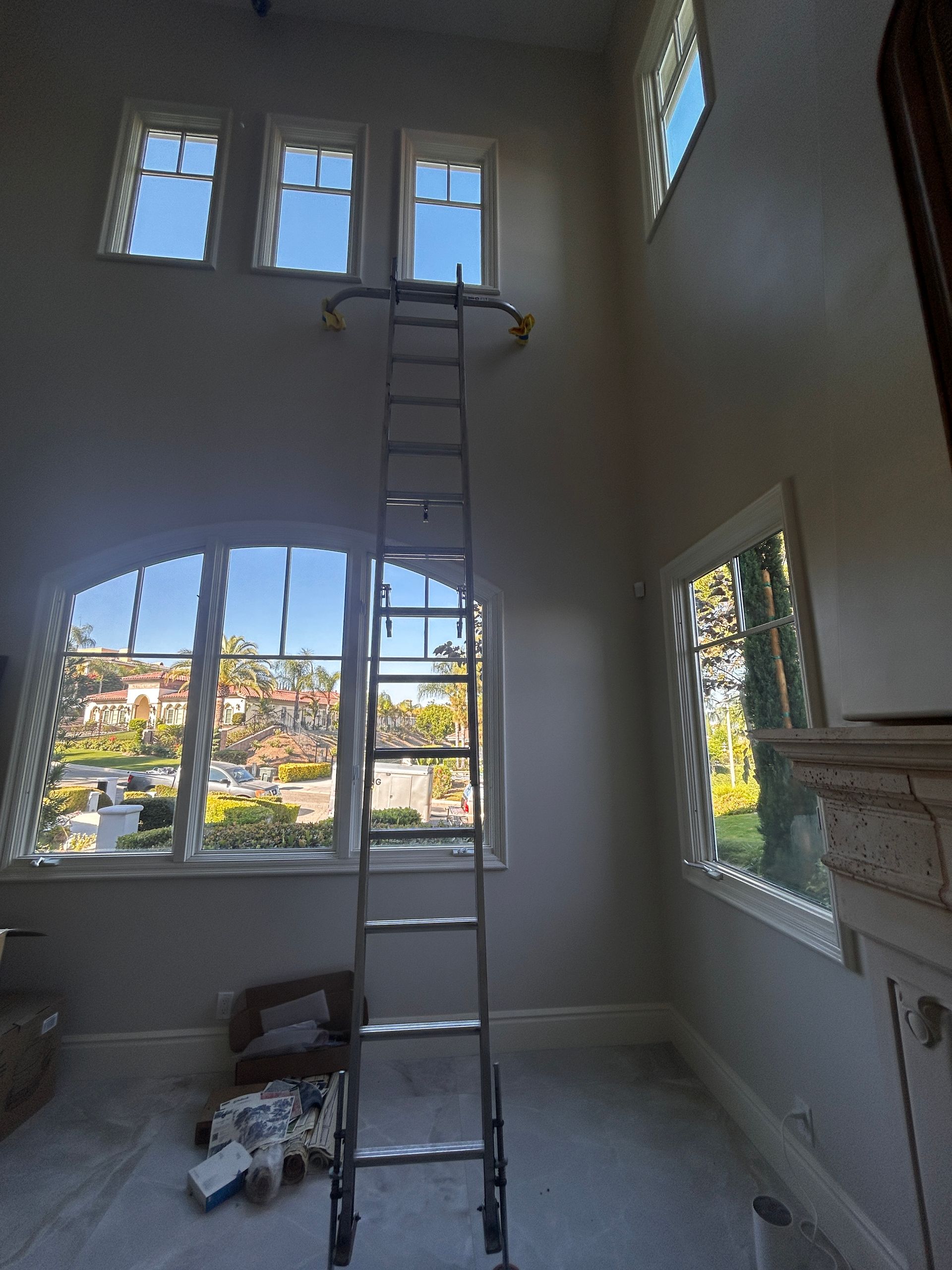 Tall ladder in a bright room with high windows and a fireplace, with painting supplies on the floor.