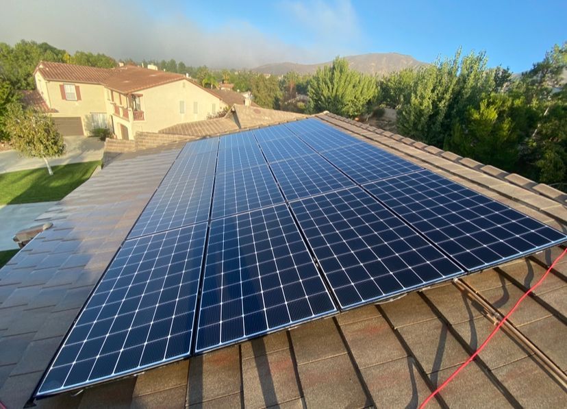 Solar panels installed on a sloped rooftop with houses and trees in the background.