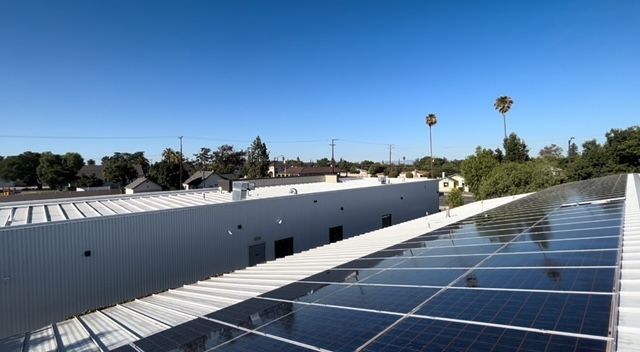Rooftop solar panels beside a white industrial building under a clear blue sky.
