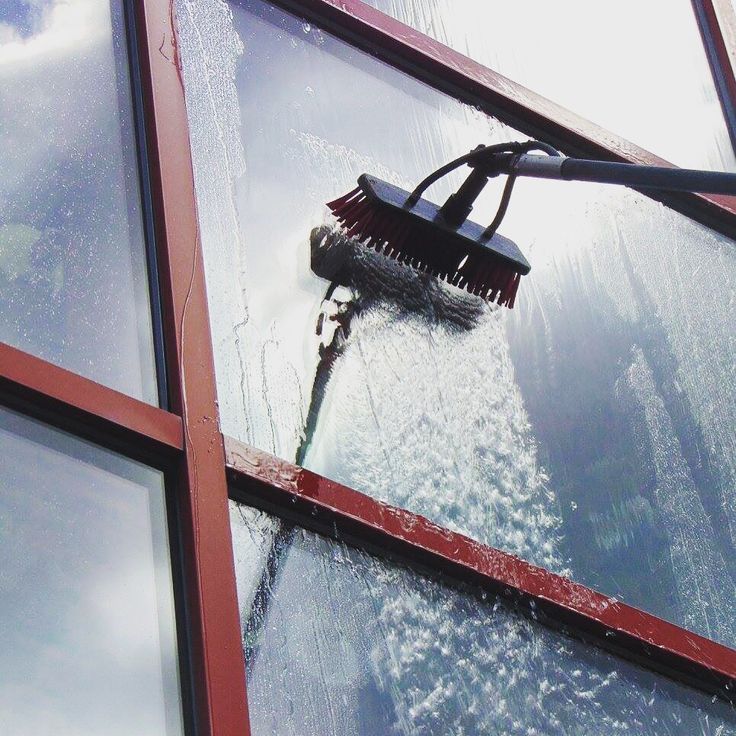 Window cleaner washing a glass facade with a long-handled brush from outside