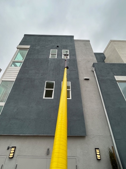 Yellow fire hose stretched up the side of a gray building toward an upper window.