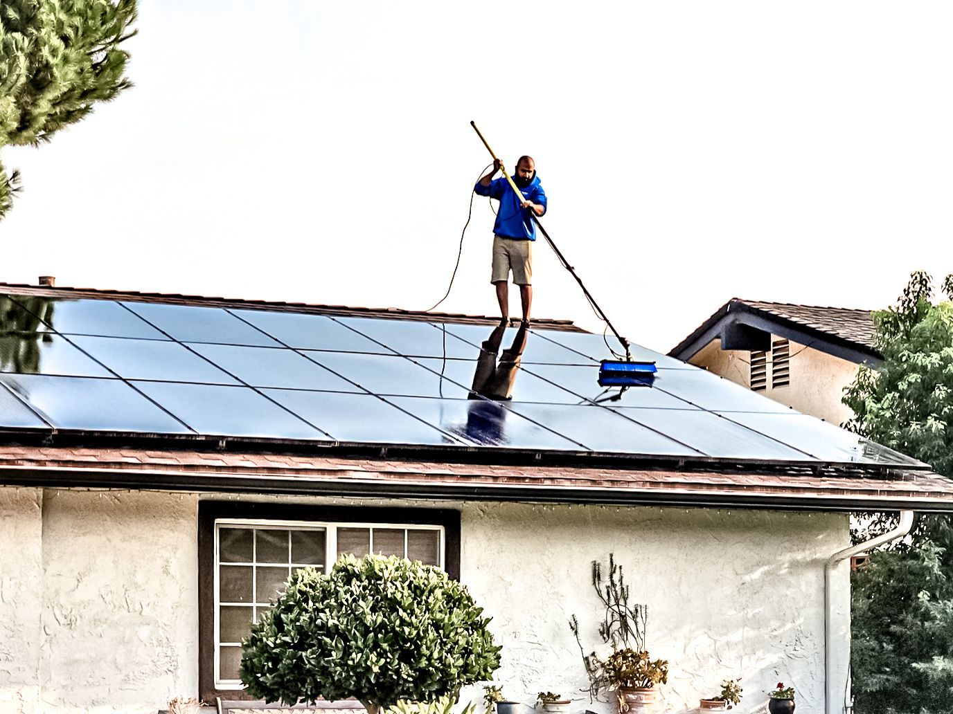 Worker cleaning solar panels on a house roof with a hose or brush