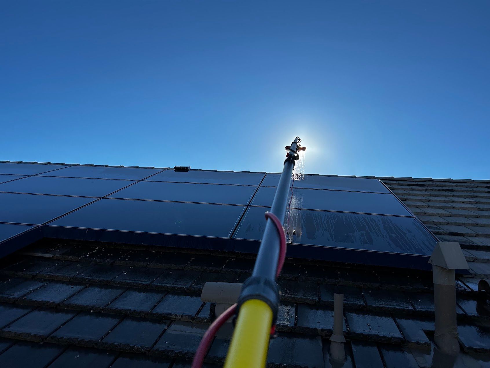 Solar panels being cleaned with a long pole under a clear blue sky.