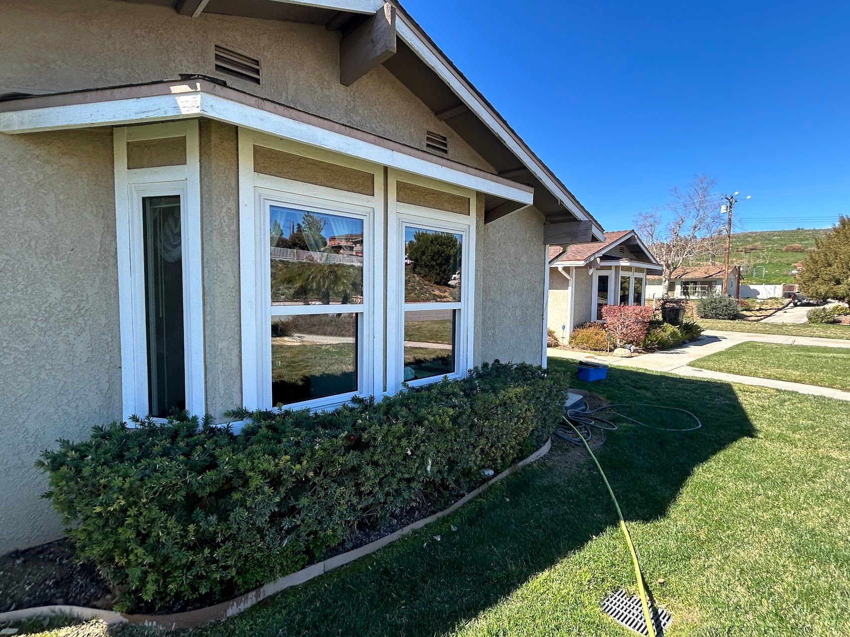 Suburban house exterior with white-trimmed windows, green shrubs, and a sunny yard.