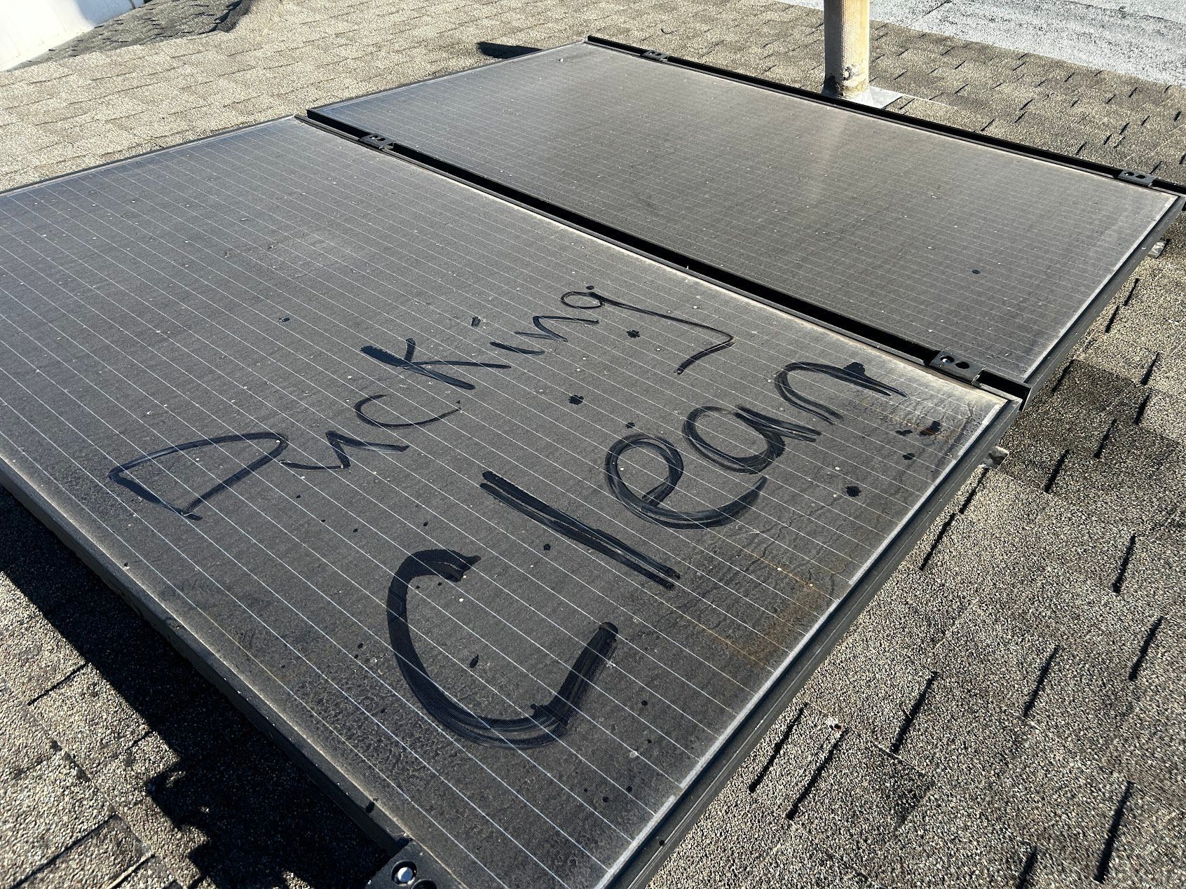 Solar panels on a roof with “Clean!” written in marker on the front panel.