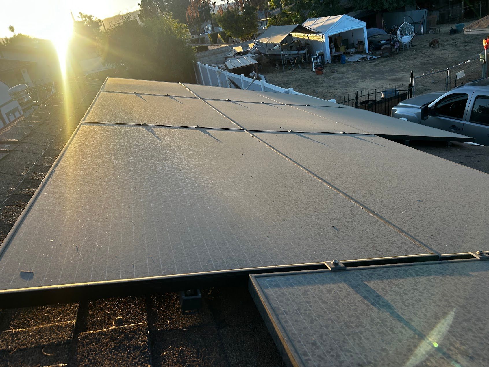dirty Rooftop solar panels at sunset, with parked vehicles and a rural yard in the background