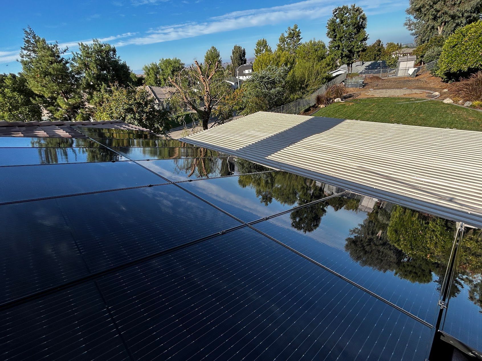 Reflective black solar panels beside a tiled pool with trees and blue sky overhead