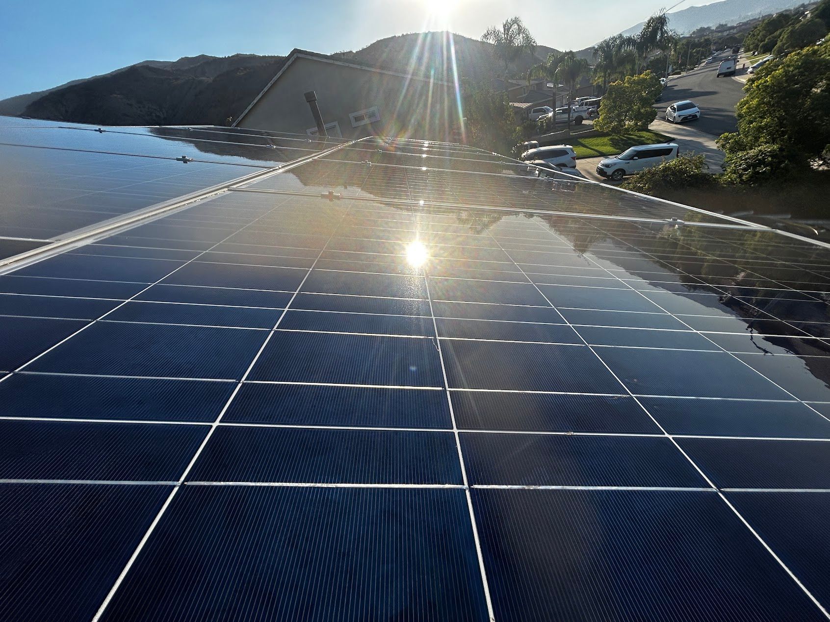 Solar panels on a roof reflecting bright sunlight with a coastal hillside in the background