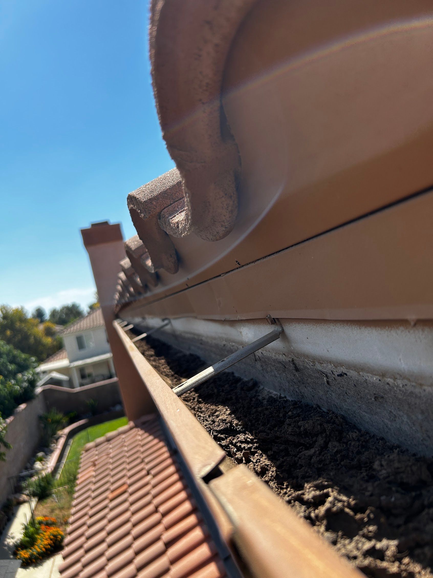 Close-up of a gutter with debris and a chipped roof edge beside red tiles Before Cleaning