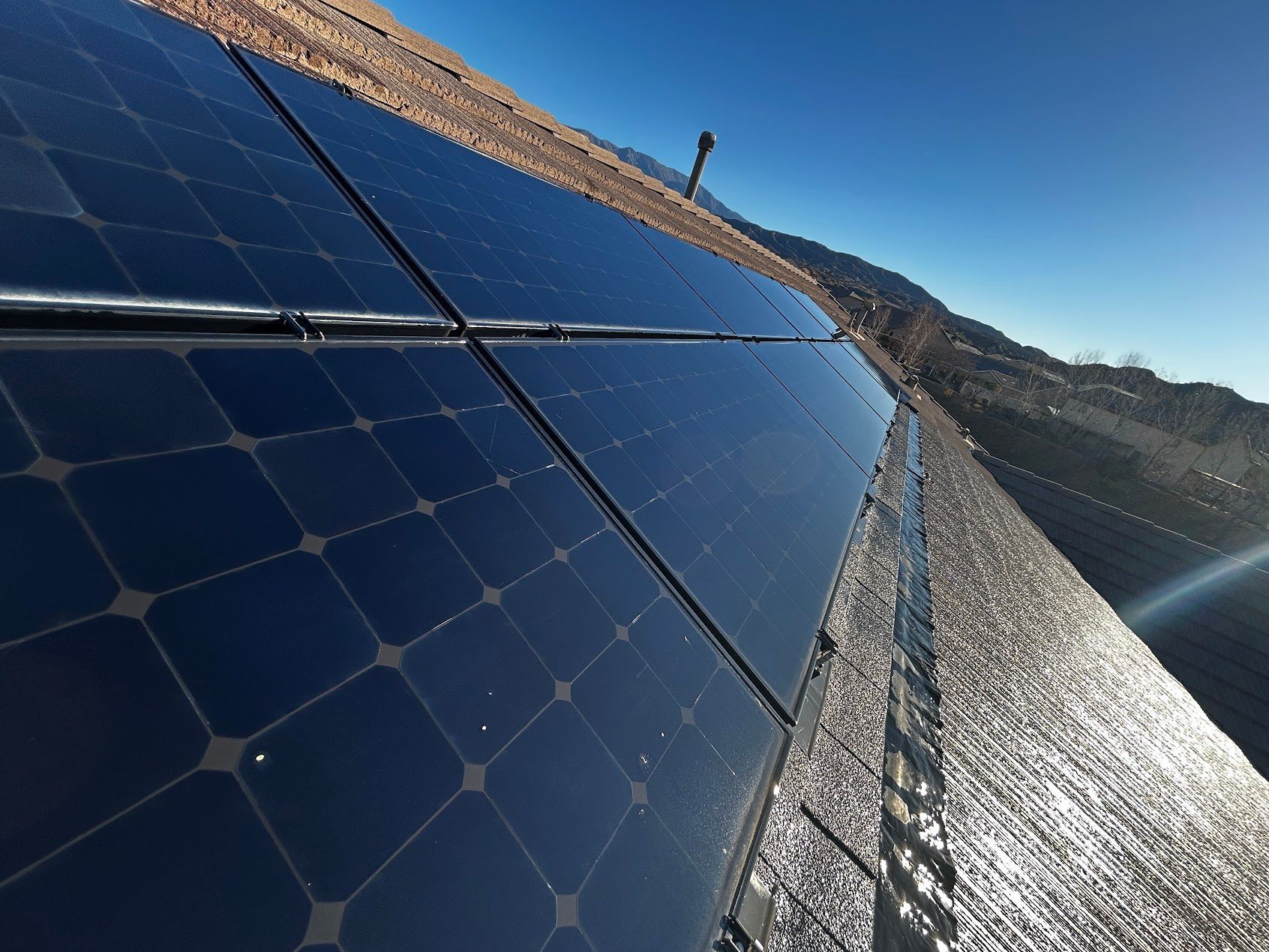 Solar panels mounted on a rooftop beside a snowy mountain under a clear blue sky