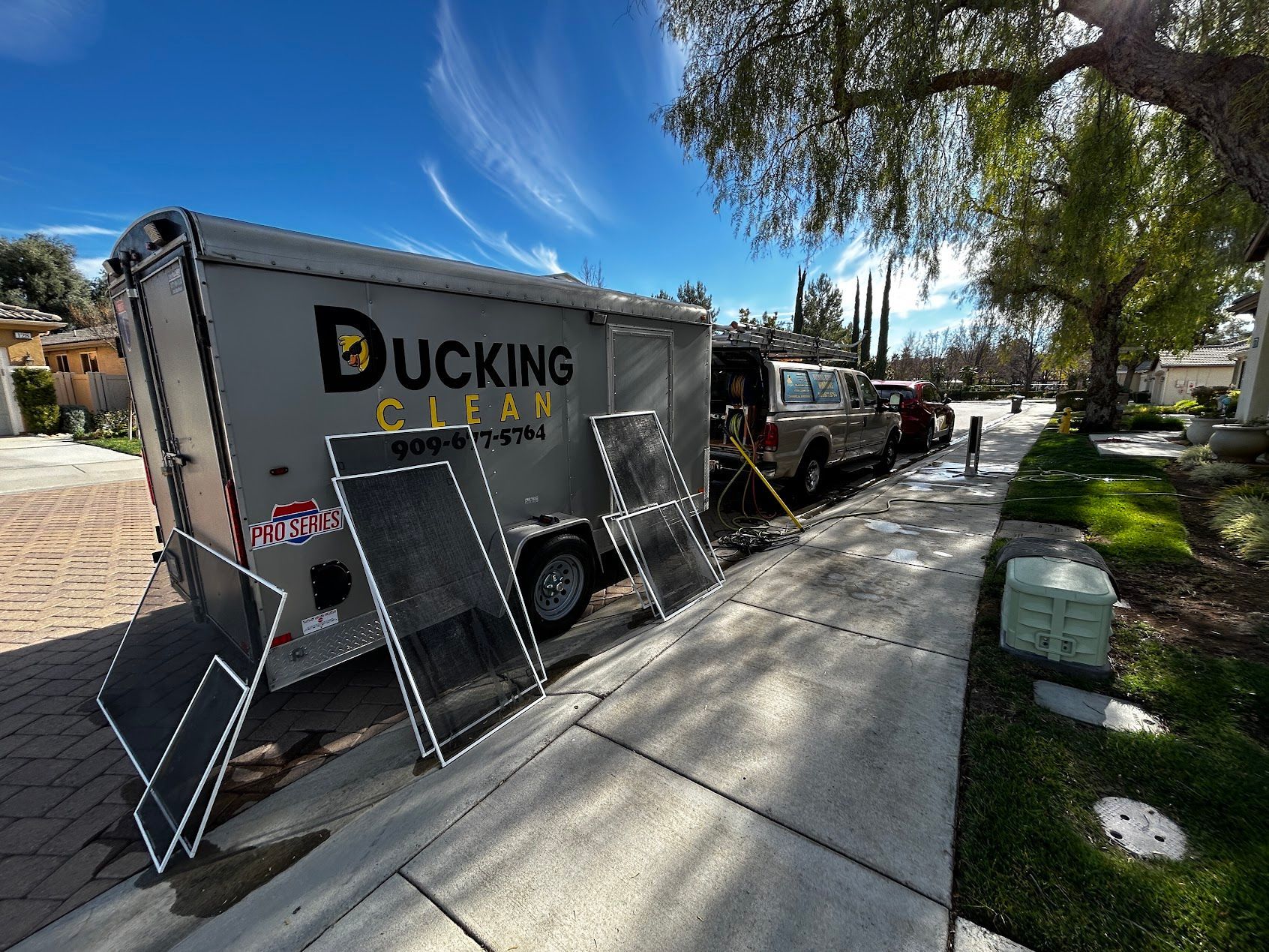 Ducking Clean truck and trailer parked on a sunny residential street with cleaning equipment nearby