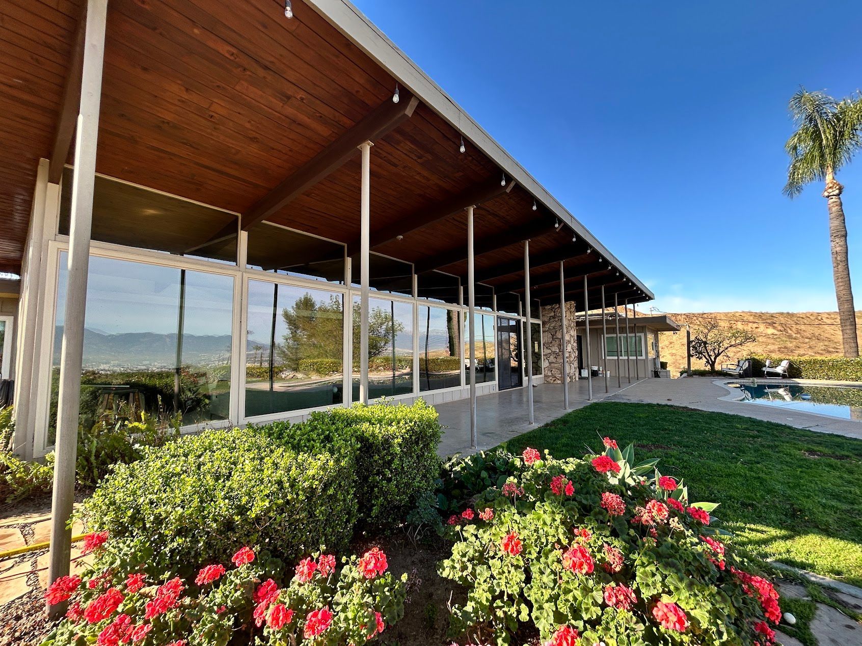 Modern building with covered patio, glass walls, and red flowers under a bright blue sky
