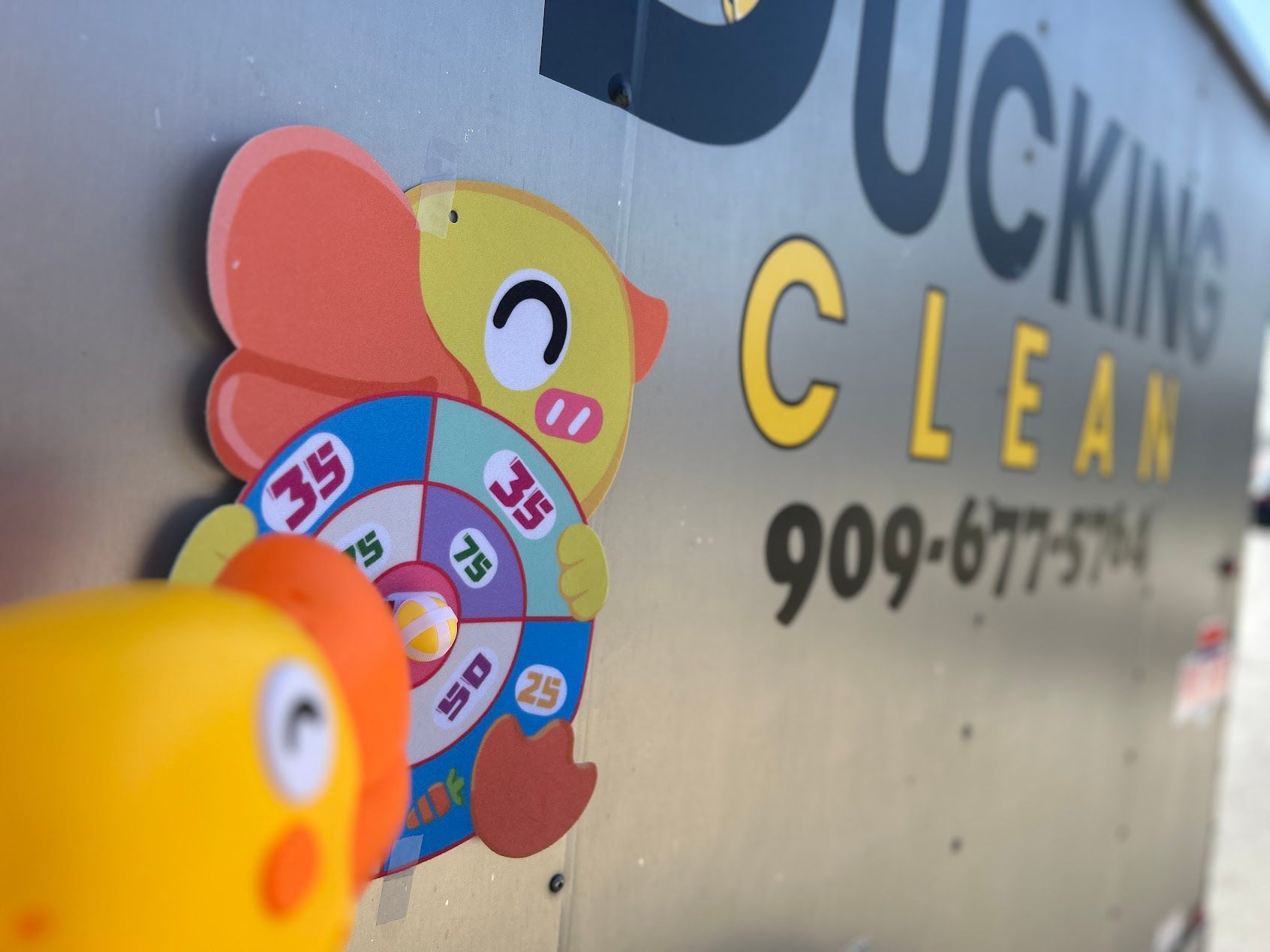 Duck Clean sign with colorful cartoon ducks on a wall, showing a phone number.