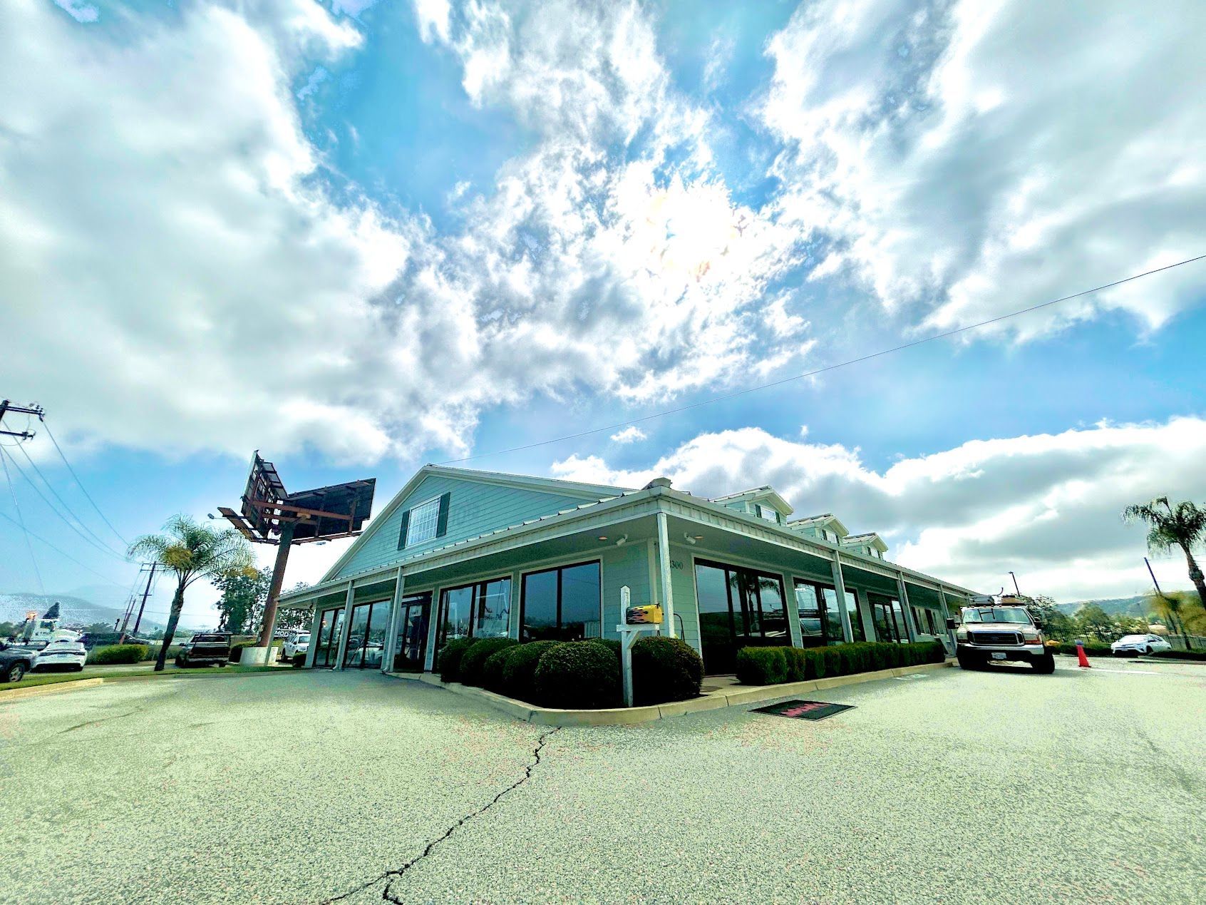 Low, white roadside diner with green roof under a bright blue sky and clouds