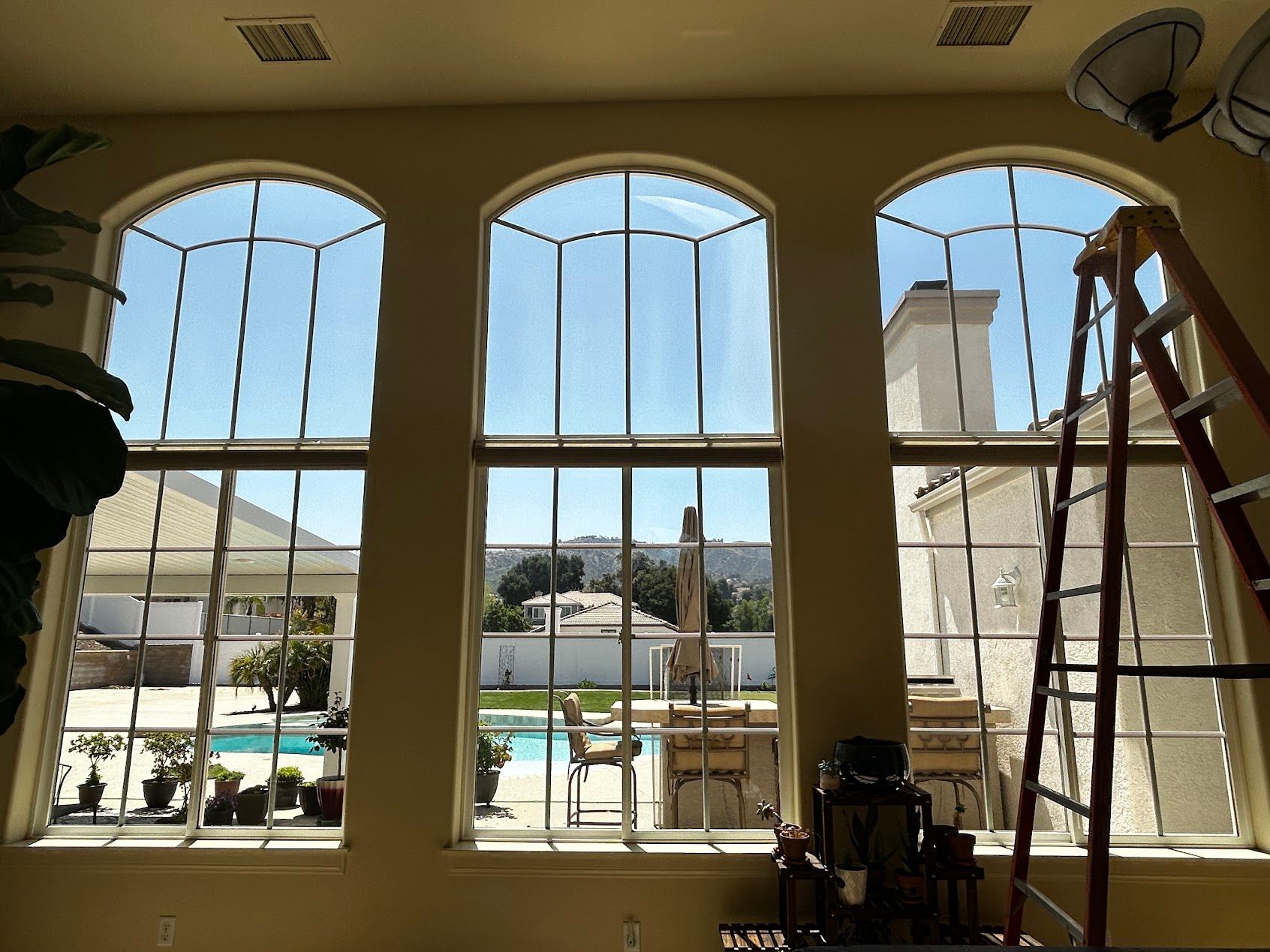Interior with three arched windows overlooking a backyard pool, with a ladder and work equipment inside.