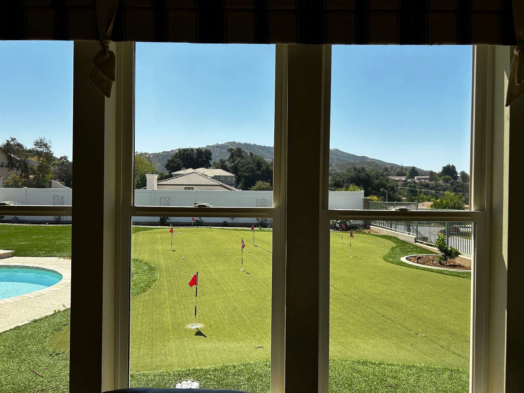 View from a window overlooking a golf course with green fairway, bunkers, and distant hills under a blue sky