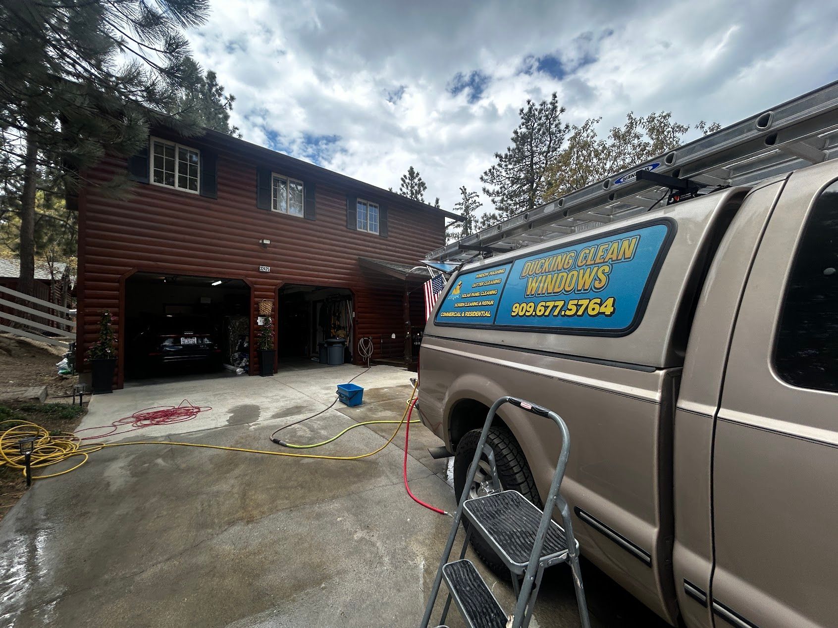 Work truck and ladder in driveway beside a two-story brown house under construction with open garage doors