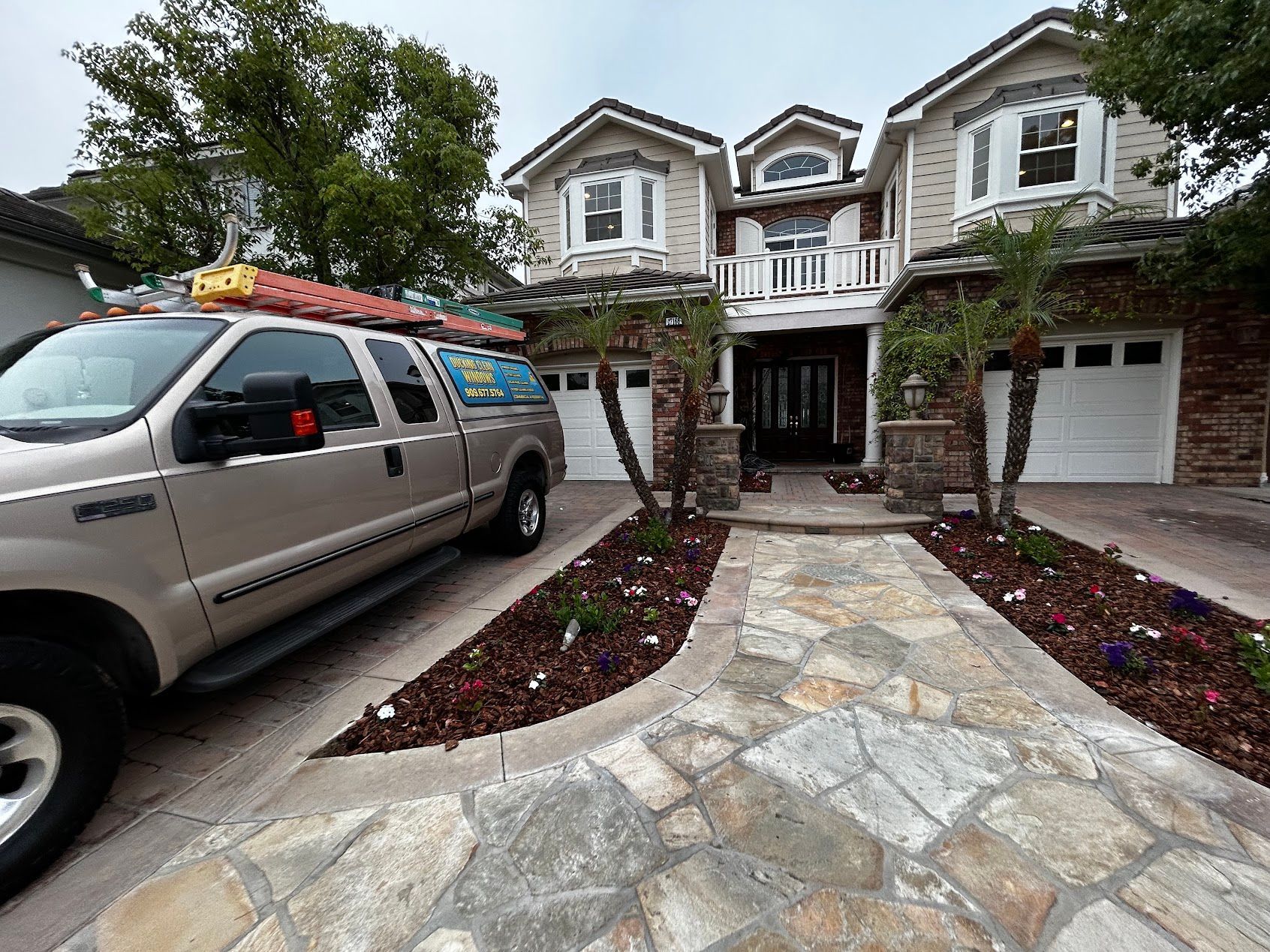 Stone driveway leading to a large house, with a work van parked on the left and landscaped flower beds.