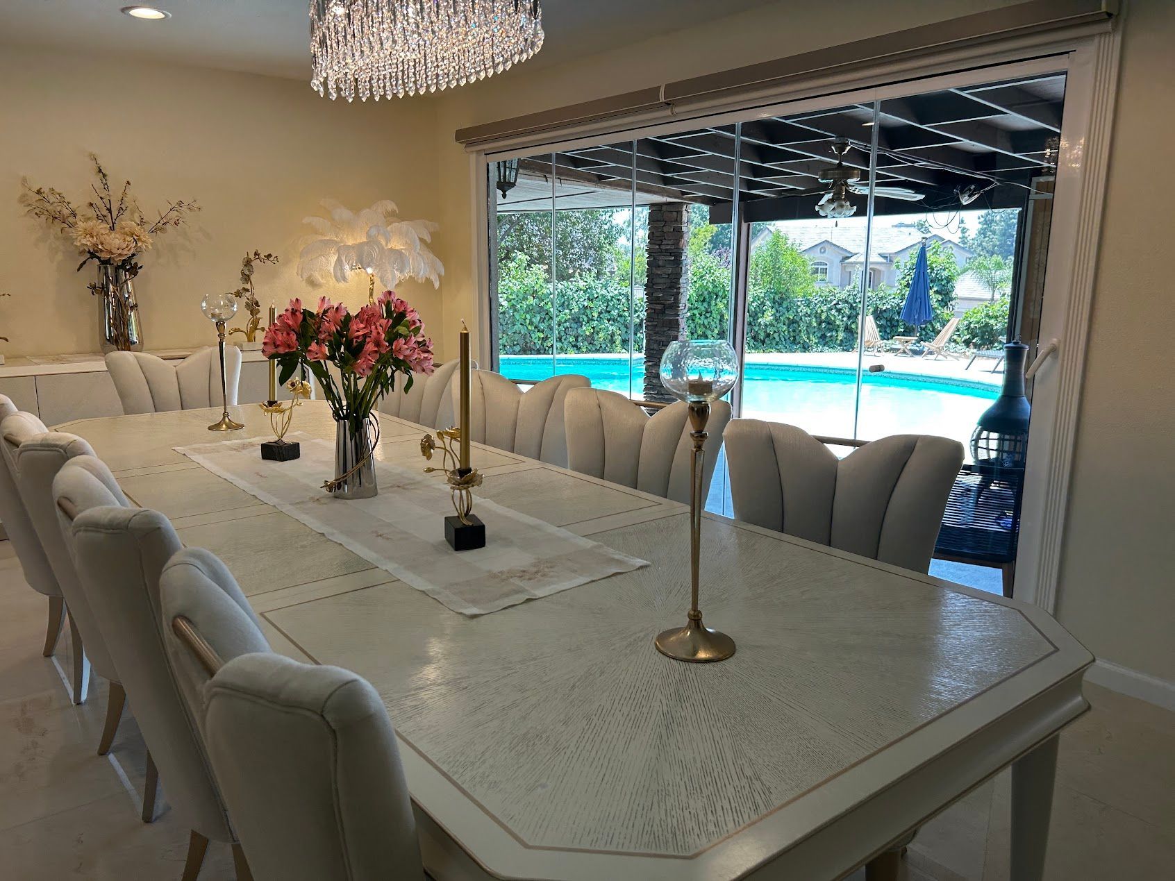 Elegant dining room with white table, chandeliers, and sliding doors opening to a patio and pool