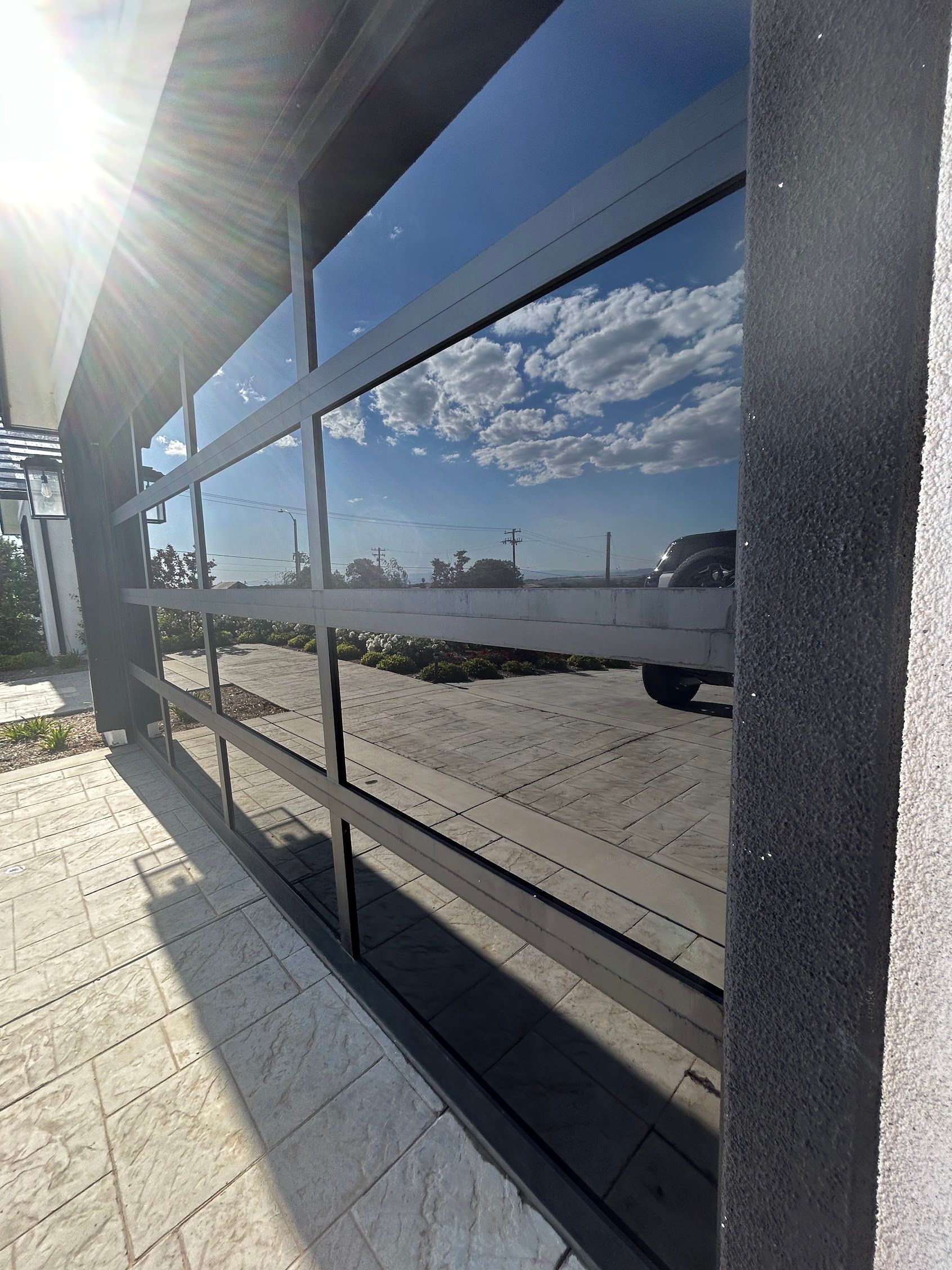 Shiny black glass wall reflecting a sunny sidewalk and cloudy sky beside a building