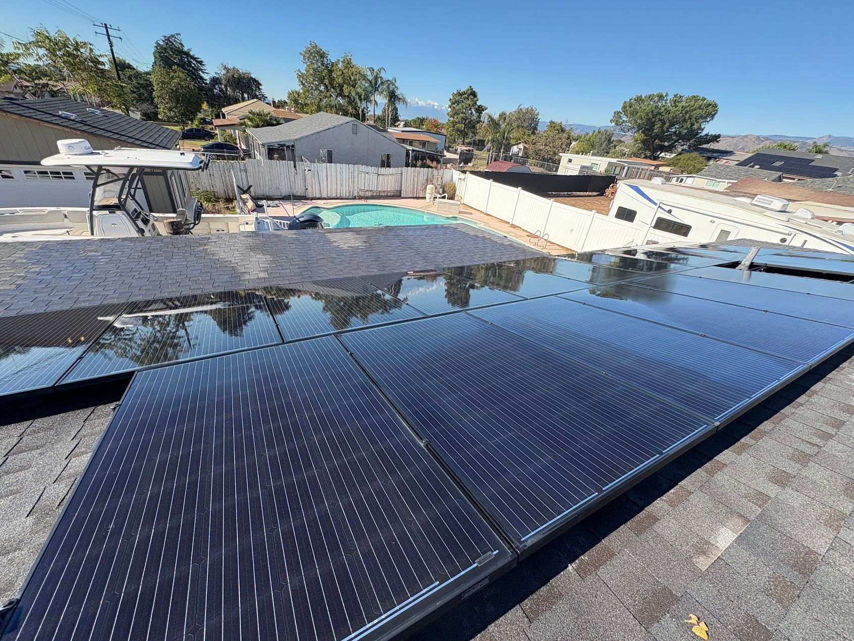 Rooftop with black solar panels beside a backyard pool and suburban homes under a clear sky