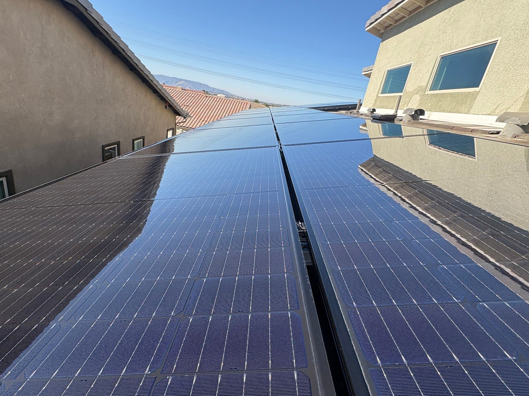 Solar panels on a rooftop between two houses under a clear blue sky.