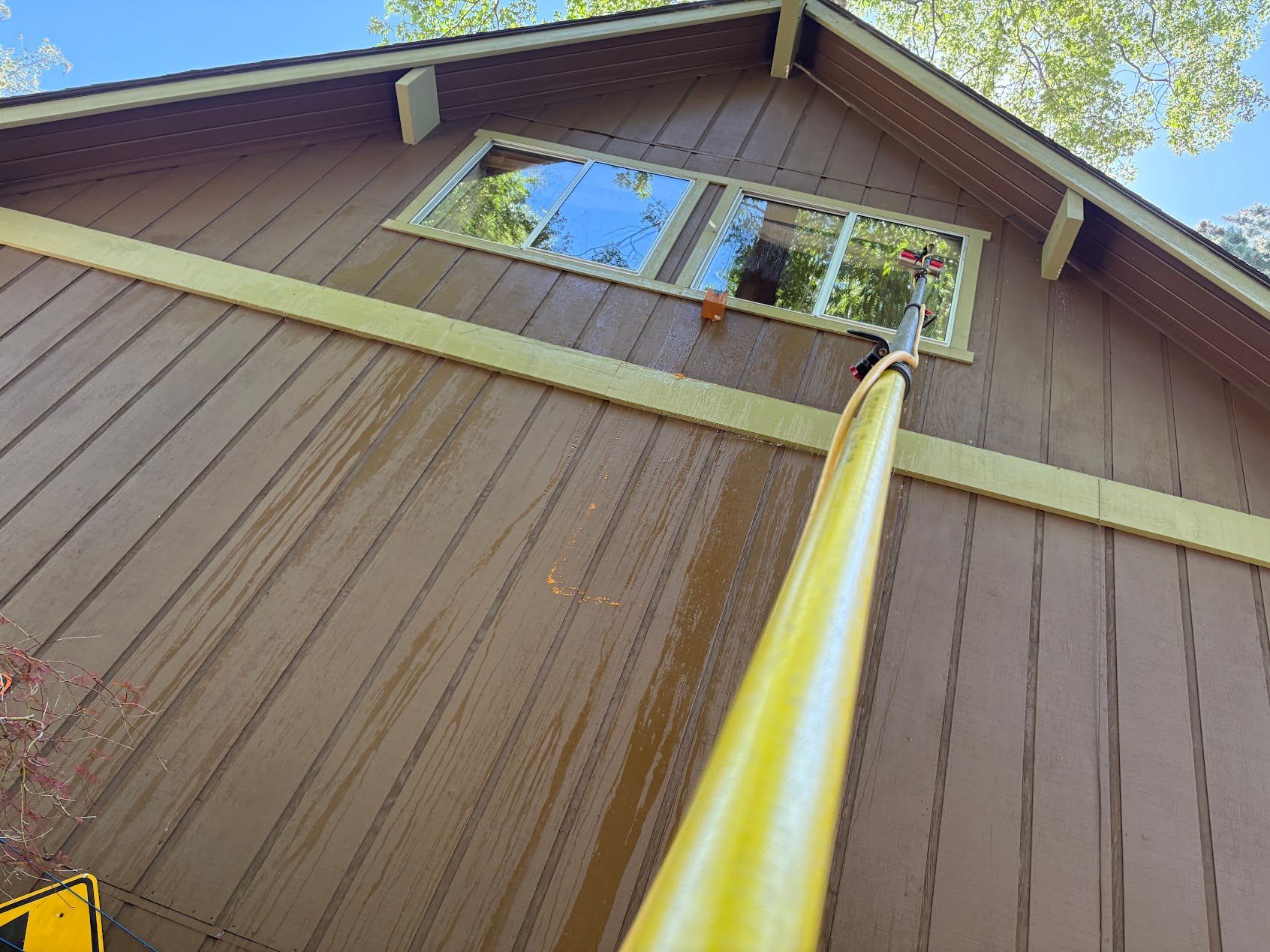 Yellow pole against brown wooden house wall, looking up toward a window and roofline.