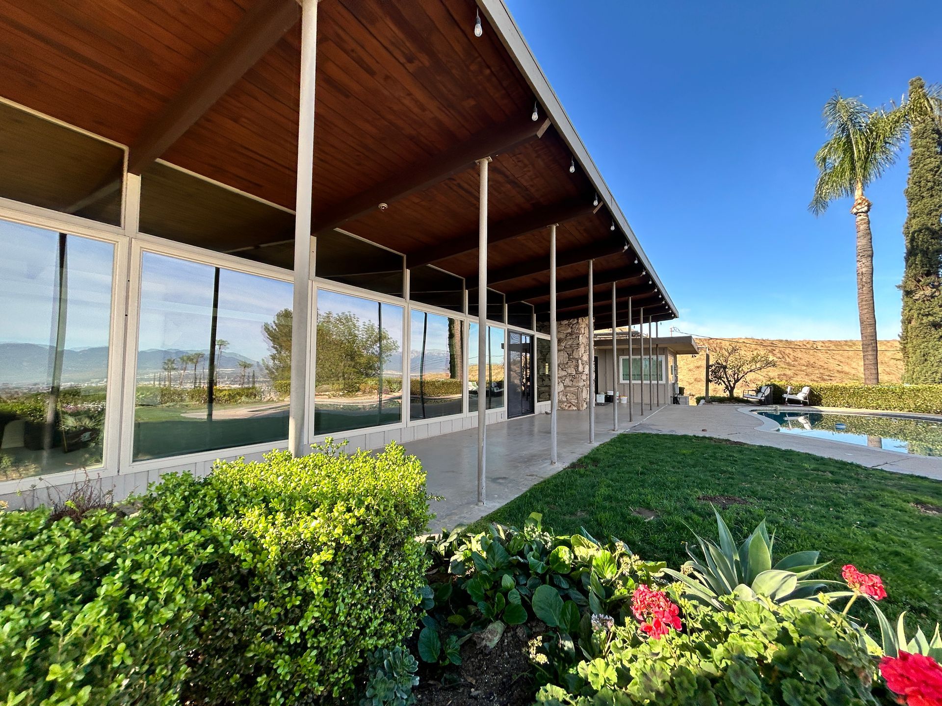 Modern building with a slanted wooden roof, glass walls, and landscaped garden under a blue sky