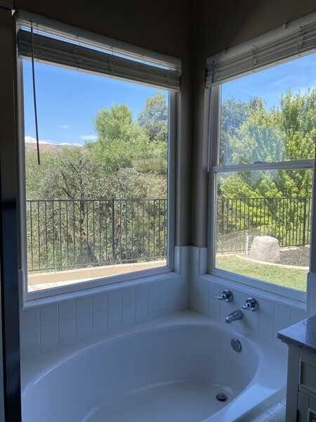 Corner bathtub beside large windows with a view of trees and blue sky